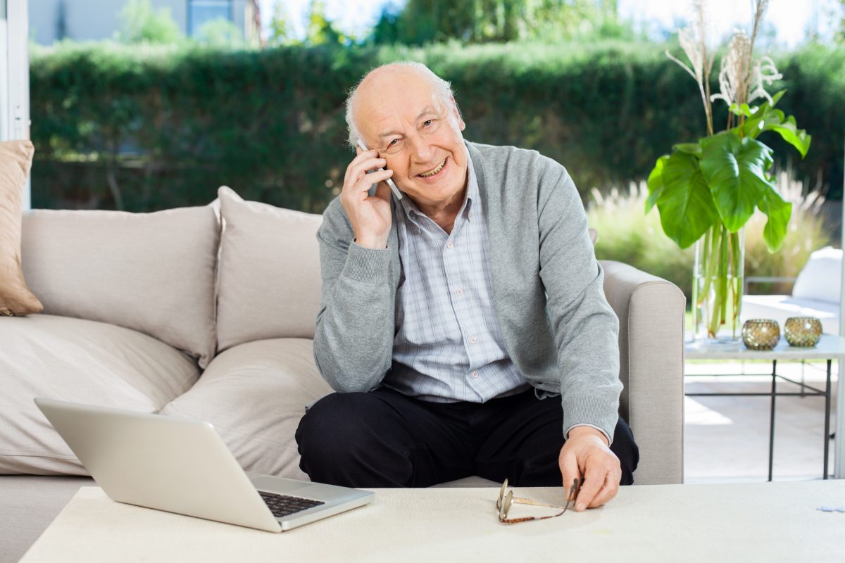 Smiling Senior Man Answering Smartphone At Nursing Home Porch